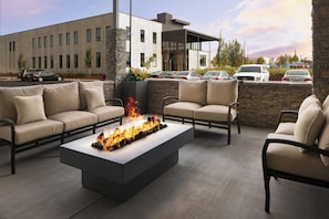 An outdoor seating area with a fire feature, stone accents, and a view of a parking lot. - Holiday Inn Express & Suites Portland Airport - Cascade Stn by IHG (Portland)