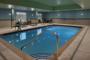Una piscina con solárium azulejado, sillas de descanso y una silla para socorrista.