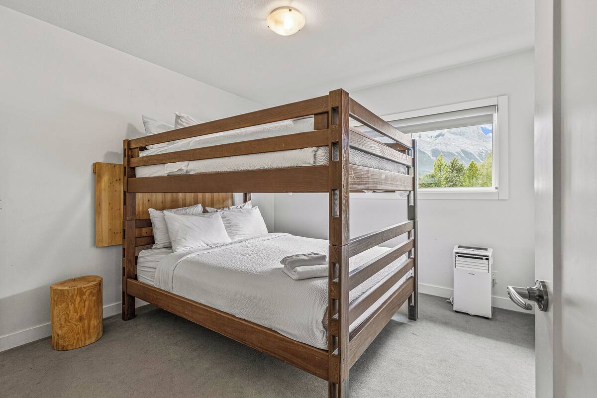 A bunk bed with a wooden frame, white bedding, and a small wooden stool.