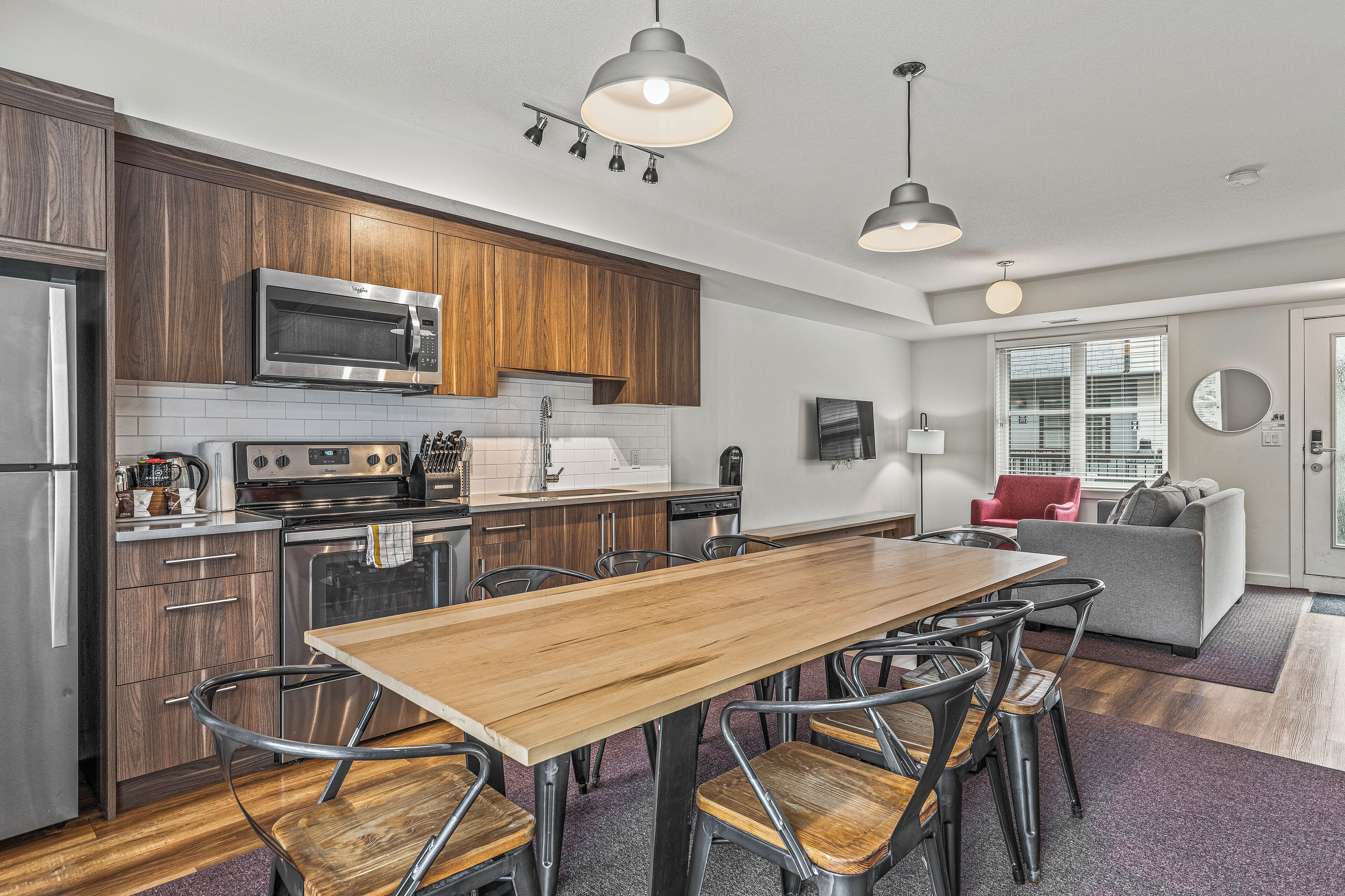 A modern kitchen with wooden cabinets, stainless steel appliances, and a dining area with a wooden table and metal chairs.