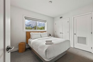 A bedroom with a bed, a window with a mountain view, a wooden stool, and a door with a vent.