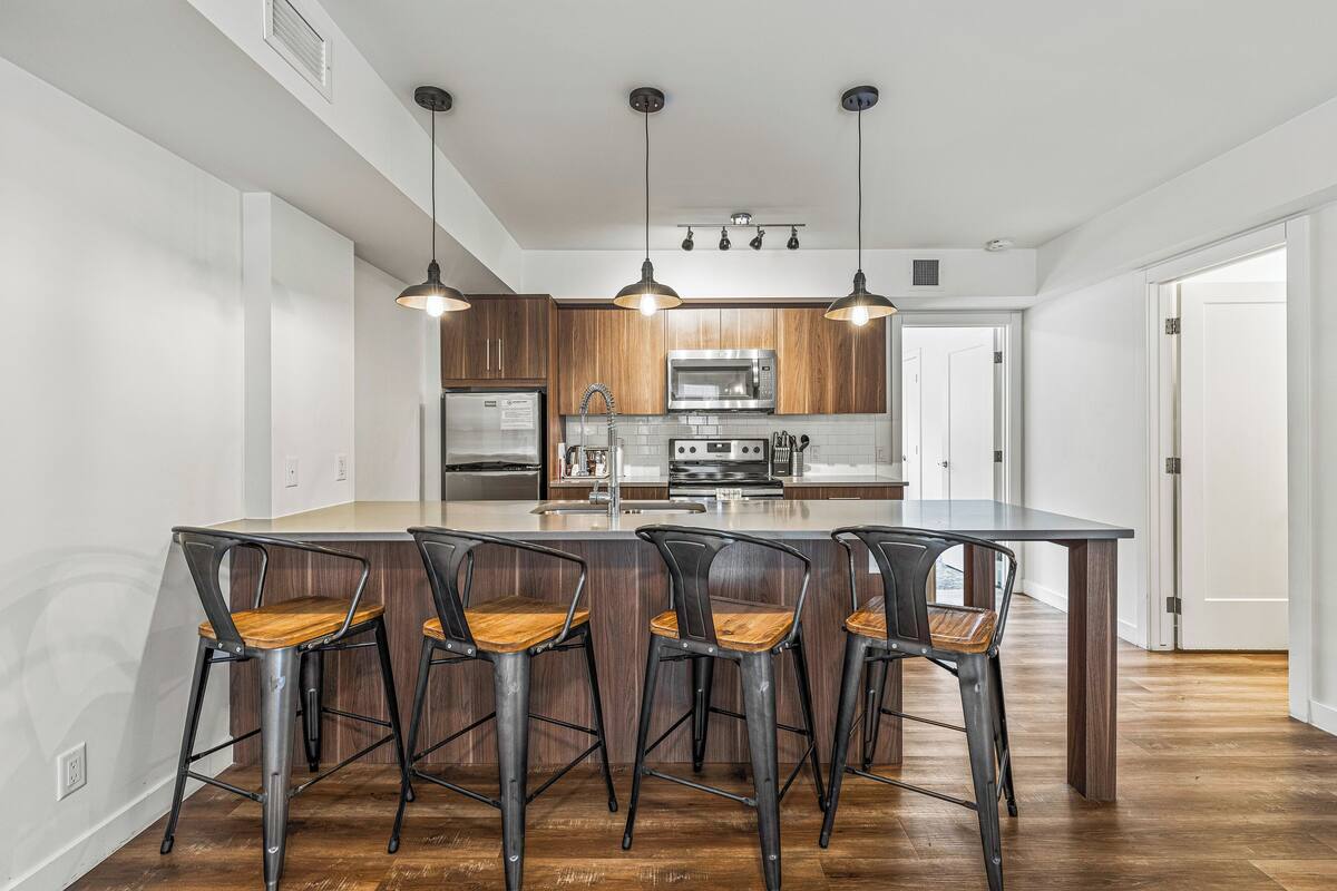 A modern kitchen with a central island, bar stools, stainless steel appliances, and pendant lighting.