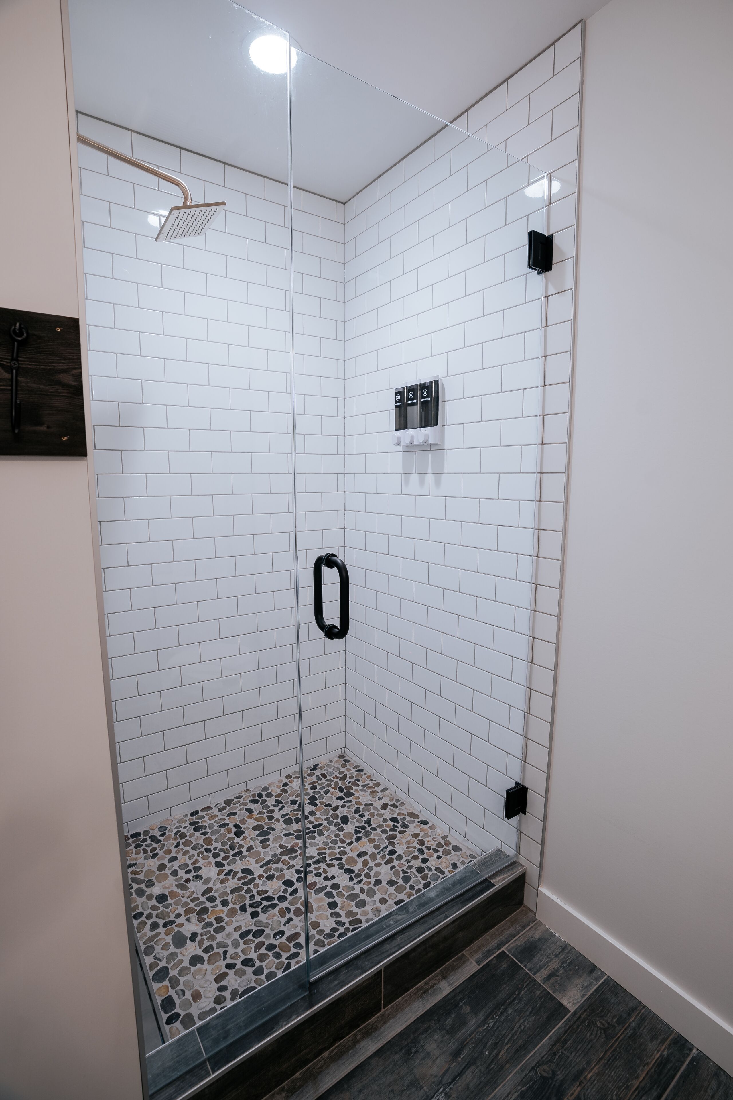 A glass-enclosed shower with white tiled walls and a pebble-patterned floor.