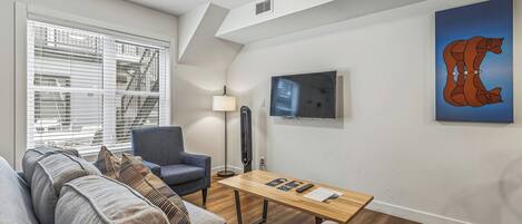 Un salon moderne avec un canapé, un fauteuil, une lampe sur pied et une table sur laquelle sont posées des télécommandes.