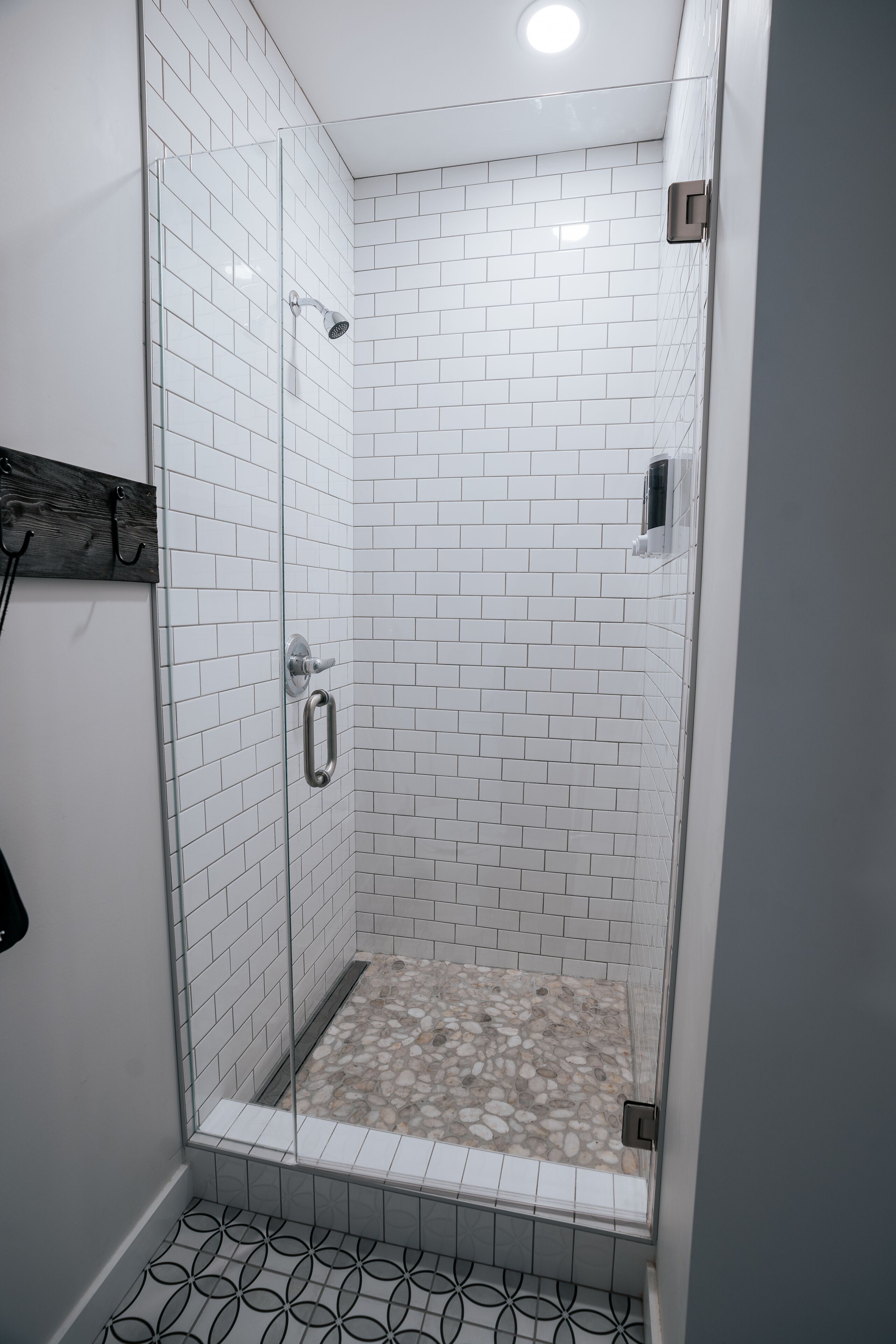 A glass-enclosed shower with white subway tiles and a pebble-patterned floor.