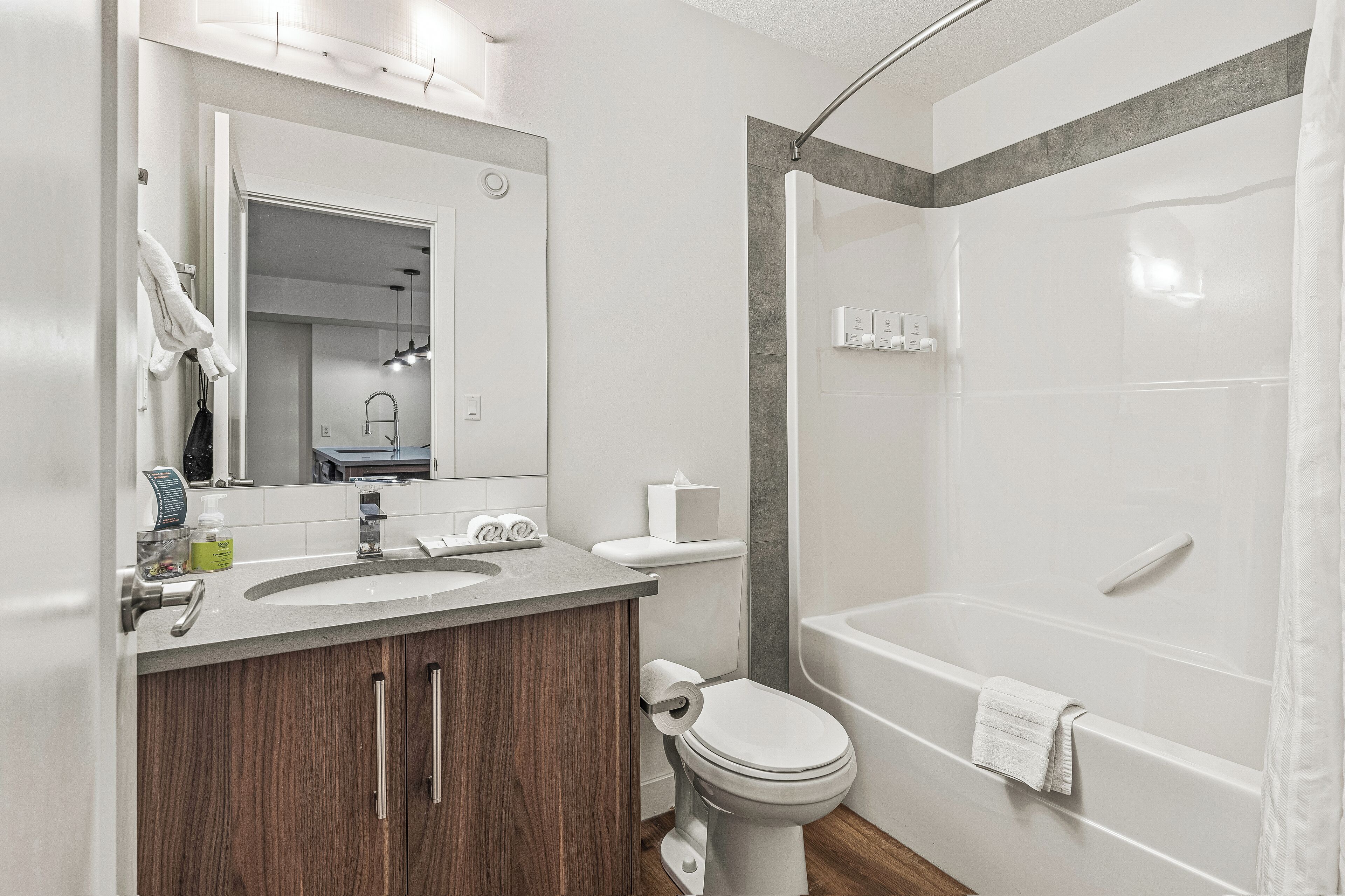 Un baño moderno con tocador de madera, inodoro, lavamanos, espejo y bañera.