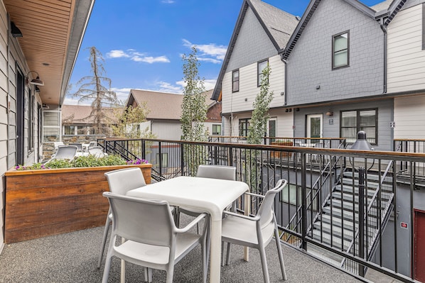 Une terrasse extérieure avec une table et des chaises, un jardinier en bois orné de fleurs et un escalier menant à un niveau supérieur.