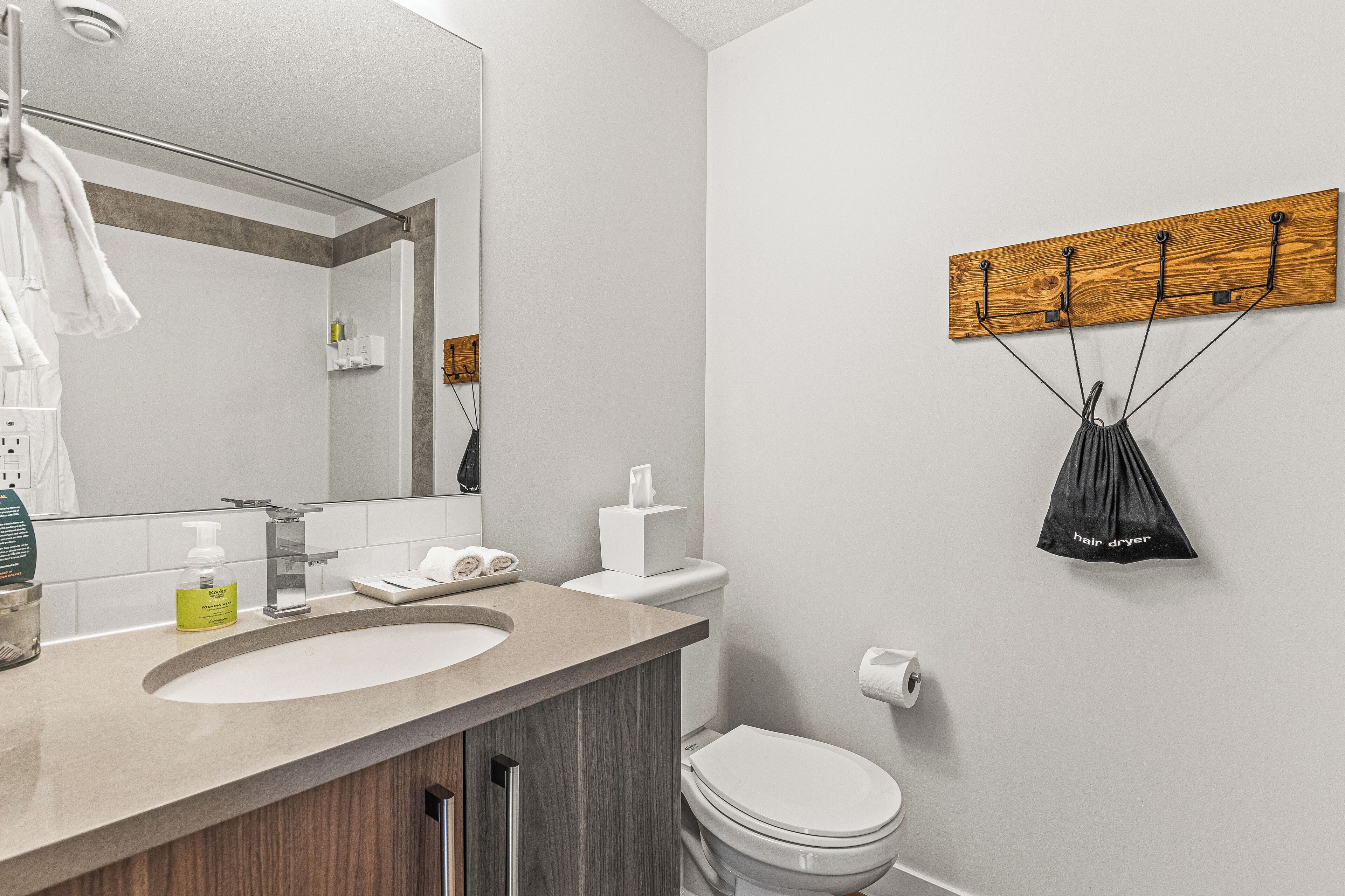 A modern bathroom with a large mirror, a sink, a toilet, and a towel rack.