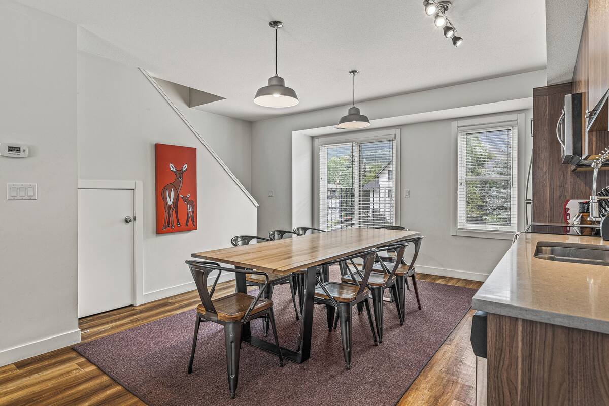 A modern kitchen with a wooden dining table, black chairs, and pendant lights.
