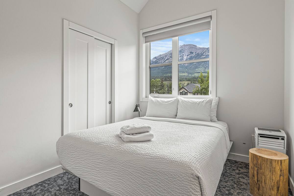 A bedroom with a bed, a window with a mountain view, a bedside table, and a nightstand.