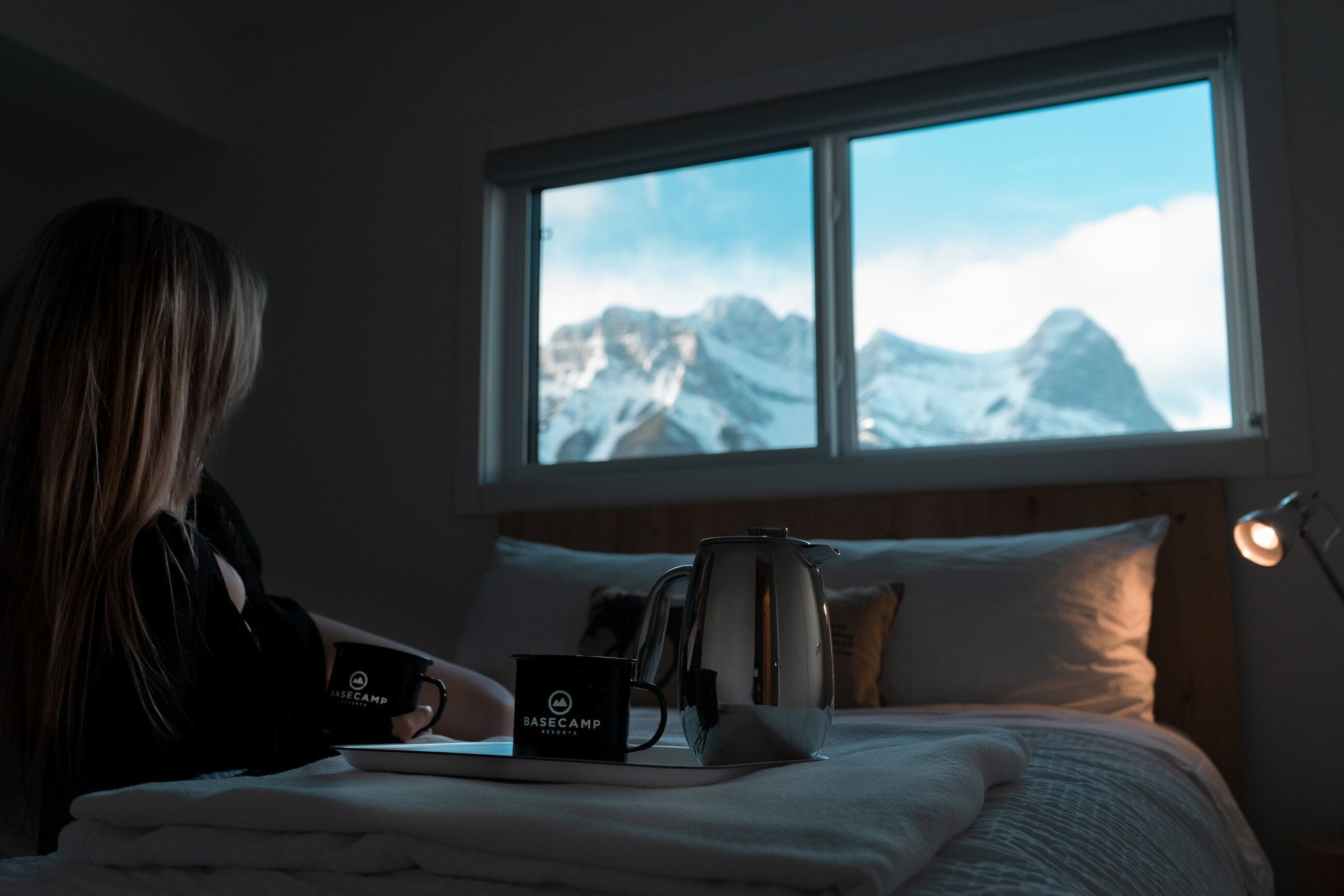 Una habitación con cama, ventana con vistas a la montaña, cafetera y taza en la mesita de noche.