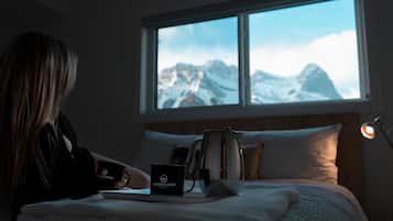 Una habitación con cama, ventana con vistas a la montaña, cafetera y taza en la mesita de noche.