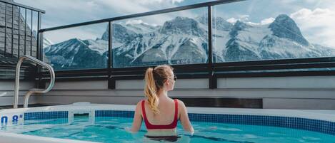 A person in a swimming pool with a view of snow-capped mountains through large windows.
