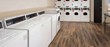 A laundry room with multiple washing machines and dryers, wooden flooring, and a door to the right.