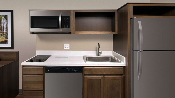 A modern kitchen with a dishwasher, stainless steel appliances, and wooden cabinetry. - WoodSpring Suites Cherry Hill (Cherry Hill)
