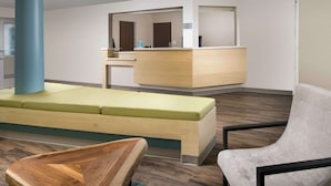 A reception area with a wooden reception desk, a seating area with a bench, and a large blue pillar. - WoodSpring Suites Cherry Hill (Cherry Hill)