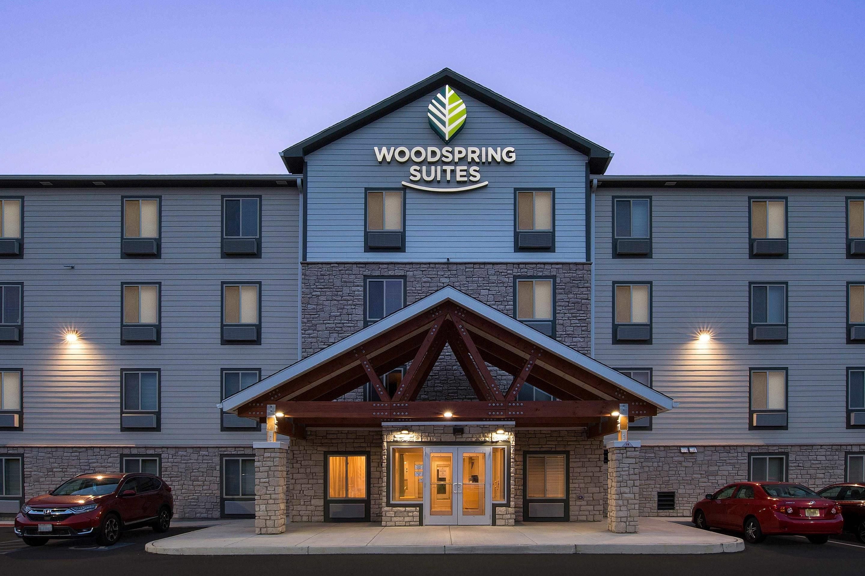 Un hôtel à plusieurs étages, reconnaissable à son grand panneau indiquant « Woodspring Suites ».