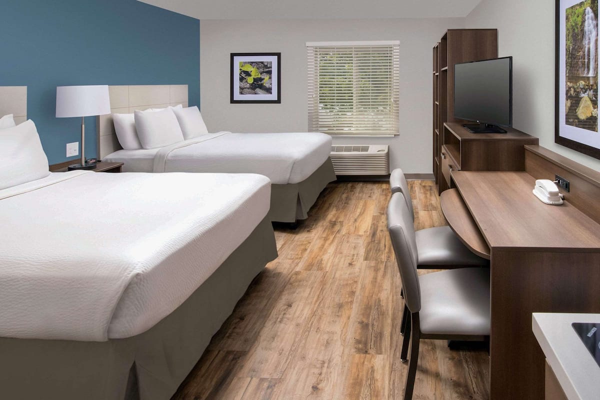 A hotel room with two beds, a desk with a chair, a TV, and a window with blinds.
