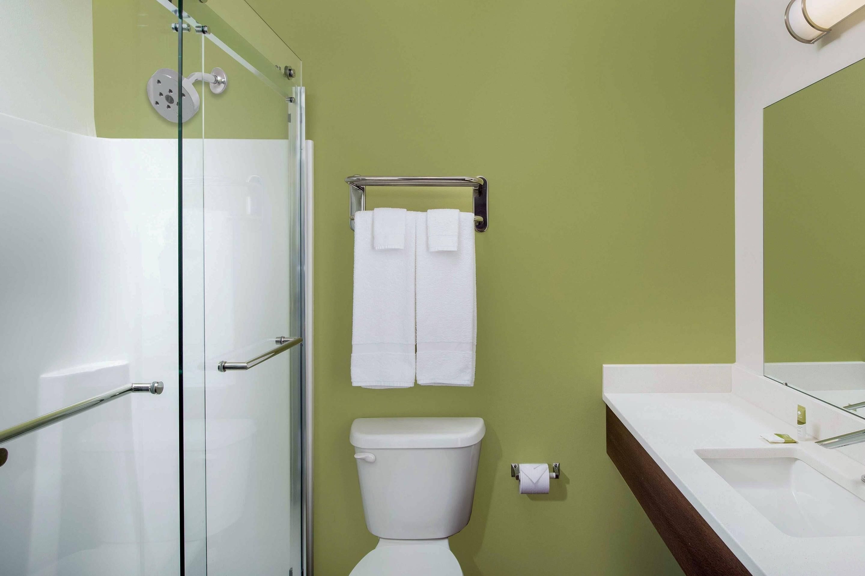 Une salle de bain avec une douche à parois de verre, des toilettes, un porte-serviettes avec deux serviettes et un lavabo avec un miroir au-dessus.
