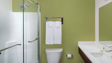 Une salle de bain avec une douche à parois de verre, des toilettes, un porte-serviettes avec deux serviettes et un lavabo avec un miroir au-dessus.