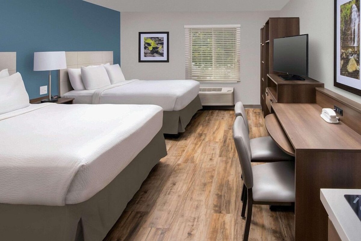 A hotel room with two beds, a desk with a chair, a television, and a framed picture on the wall.