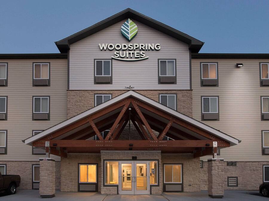 A hotel with a prominent sign reading 'WOODSPRING SUITES' and a large entrance with a covered walkway.