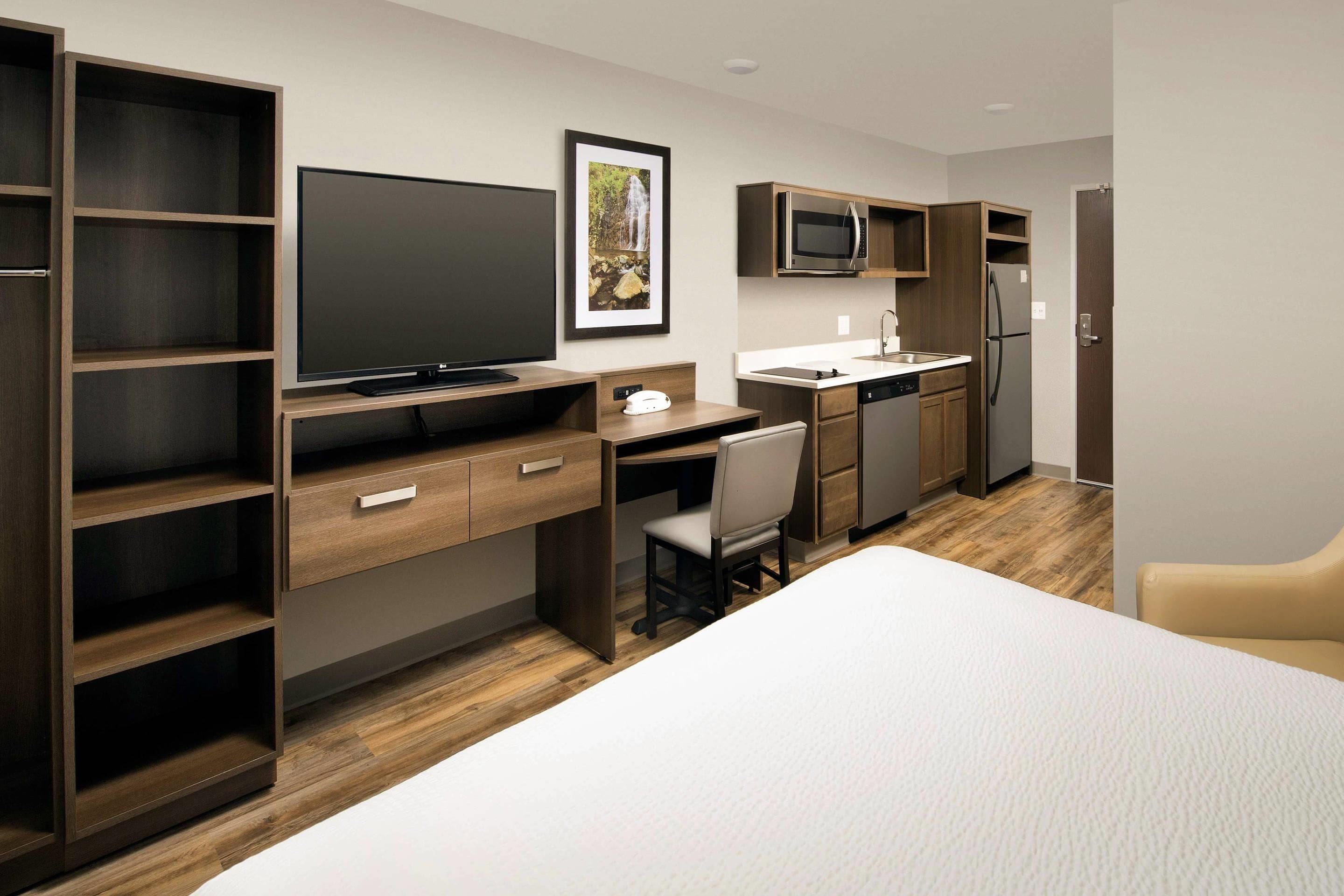 Une chambre d’hôtel de taille réduite comprenant un lit, un bureau avec une chaise, une télévision, un four à micro-ondes, un réfrigérateur et un évier.