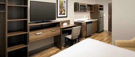 A modern hotel room with a large bed, a desk with a computer, a TV, a microwave, a refrigerator, and a small kitchenette.