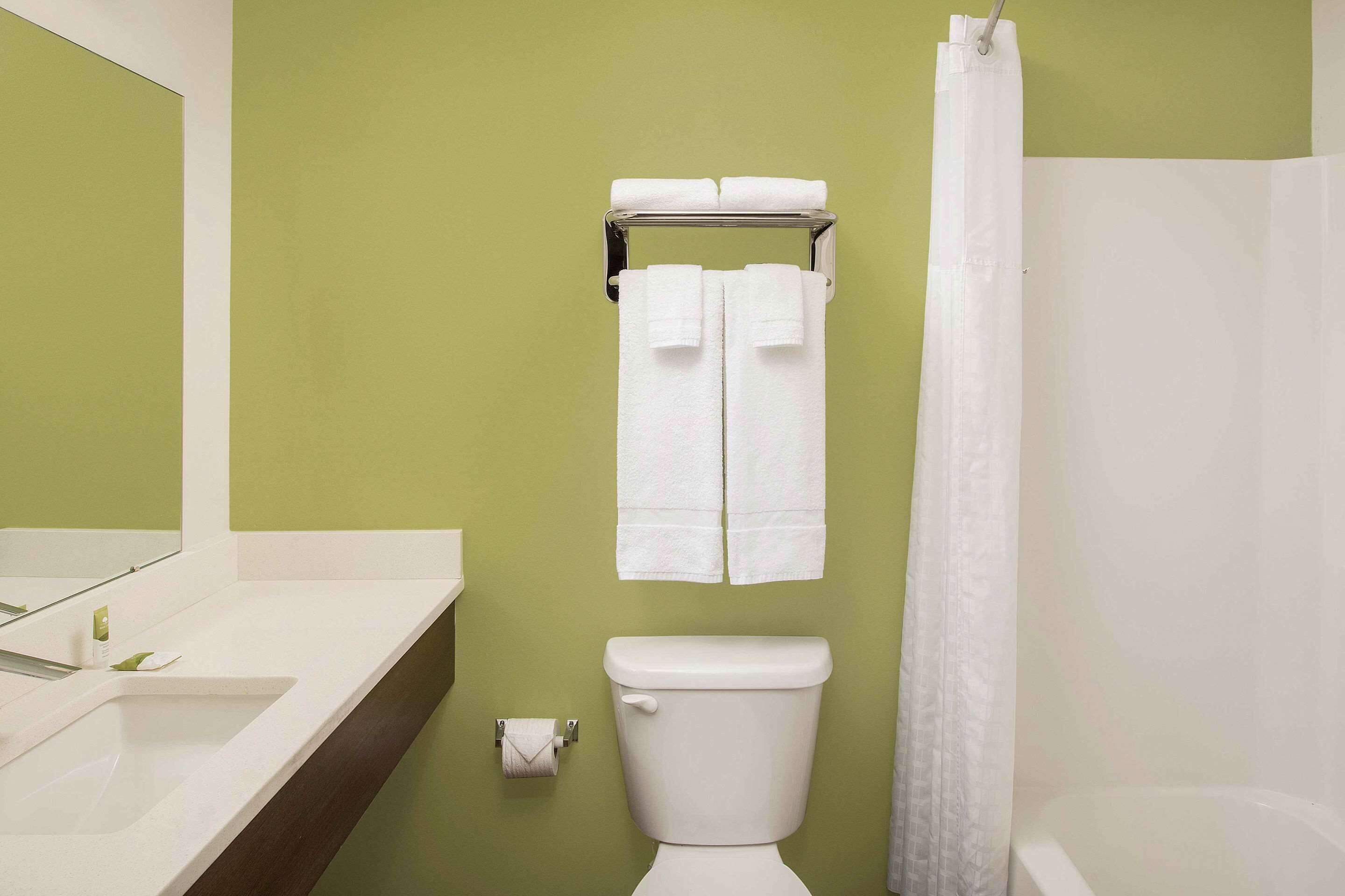 A bathroom with a green wall, white fixtures, a toilet, a sink, and a shower curtain.