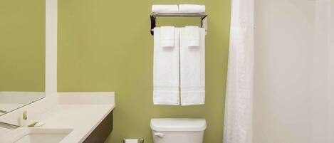 Un baño con pared verde, sanitarios y grifería blancos, inodoro, lavabo y cortina de ducha.