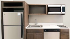 A compact kitchen with a built-in microwave, a refrigerator, a sink, and a dishwasher. - WoodSpring Suites South Plainfield (South Plainfield)