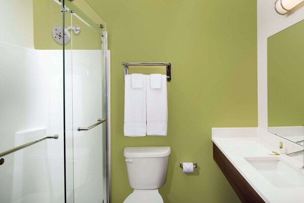 Un baño con cabina de ducha de vidrio, inodoro y lavamanos blancos, y un espejo sobre el lavamanos.