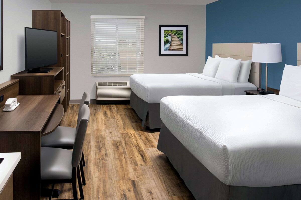 A hotel room with a wooden desk, two beds, a TV, and a picture on the wall.