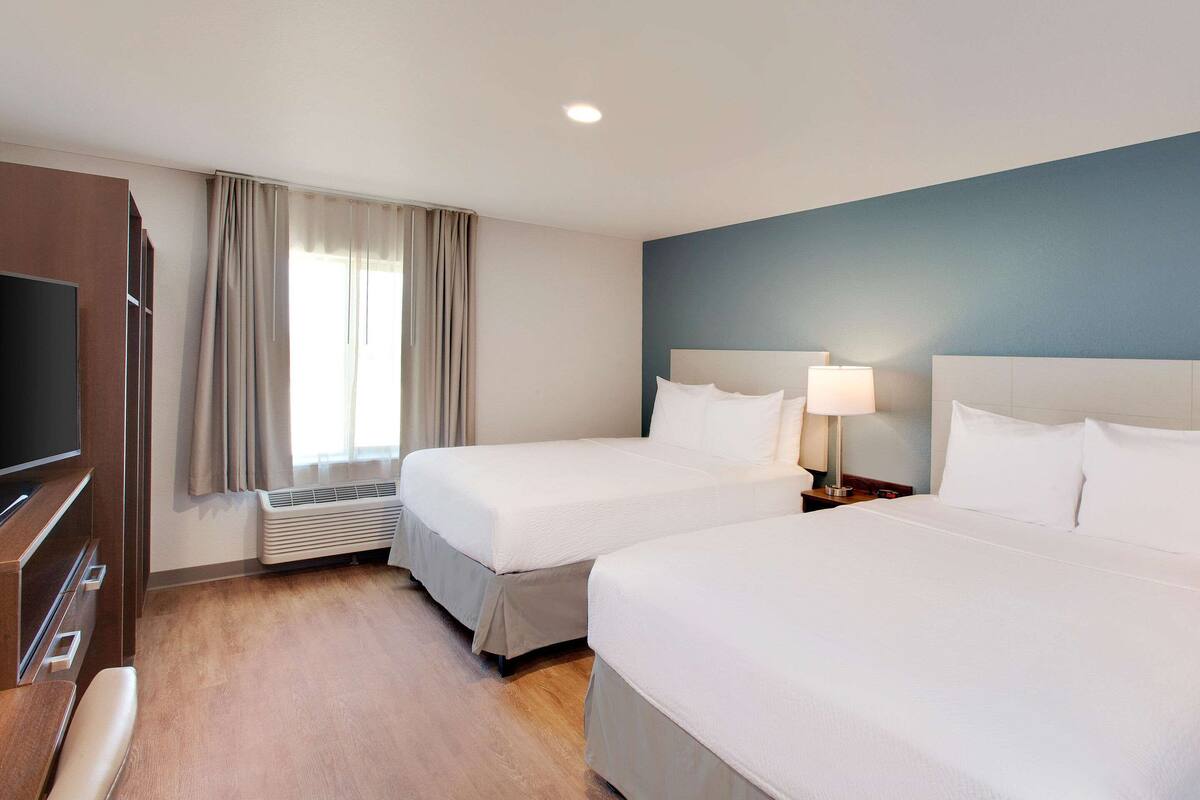 A hotel room with two beds, a TV, and an air conditioning unit.