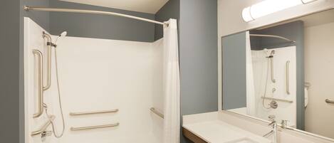 A modern bathroom with a walk-in shower, grab bars, a large mirror, and a vanity with a sink.