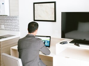 A man in a suit sitting at a desk with a laptop, a smartphone, and a pair of glasses. - WoodSpring Suites Houston Northwest (Houston)