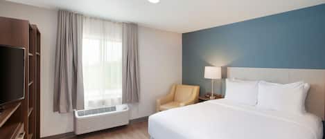 Una habitación de hotel con cama, televisión, sillón y ventana con cortinas.