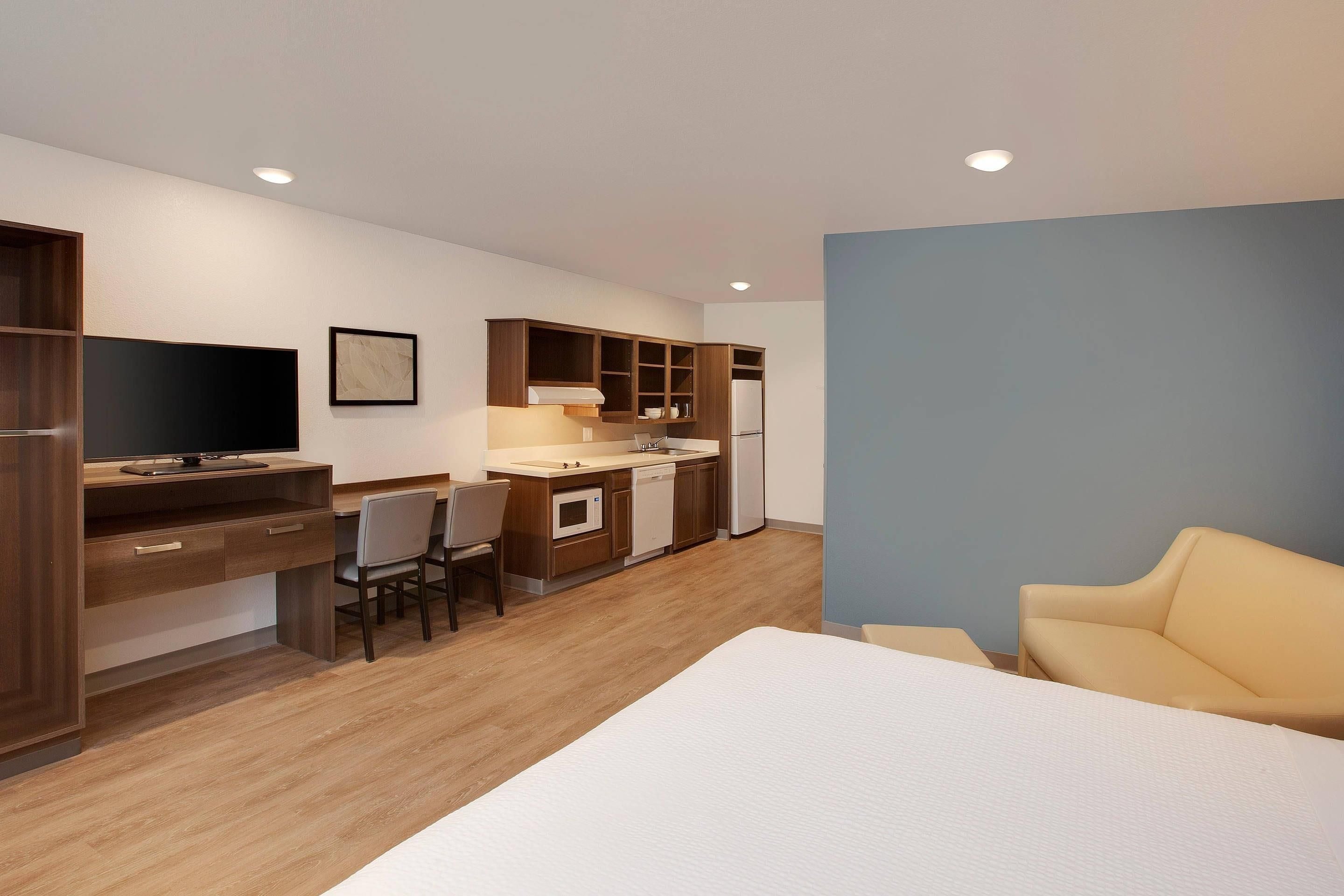 A compact hotel room with a kitchenette, a dining area, a bed, and a seating area.