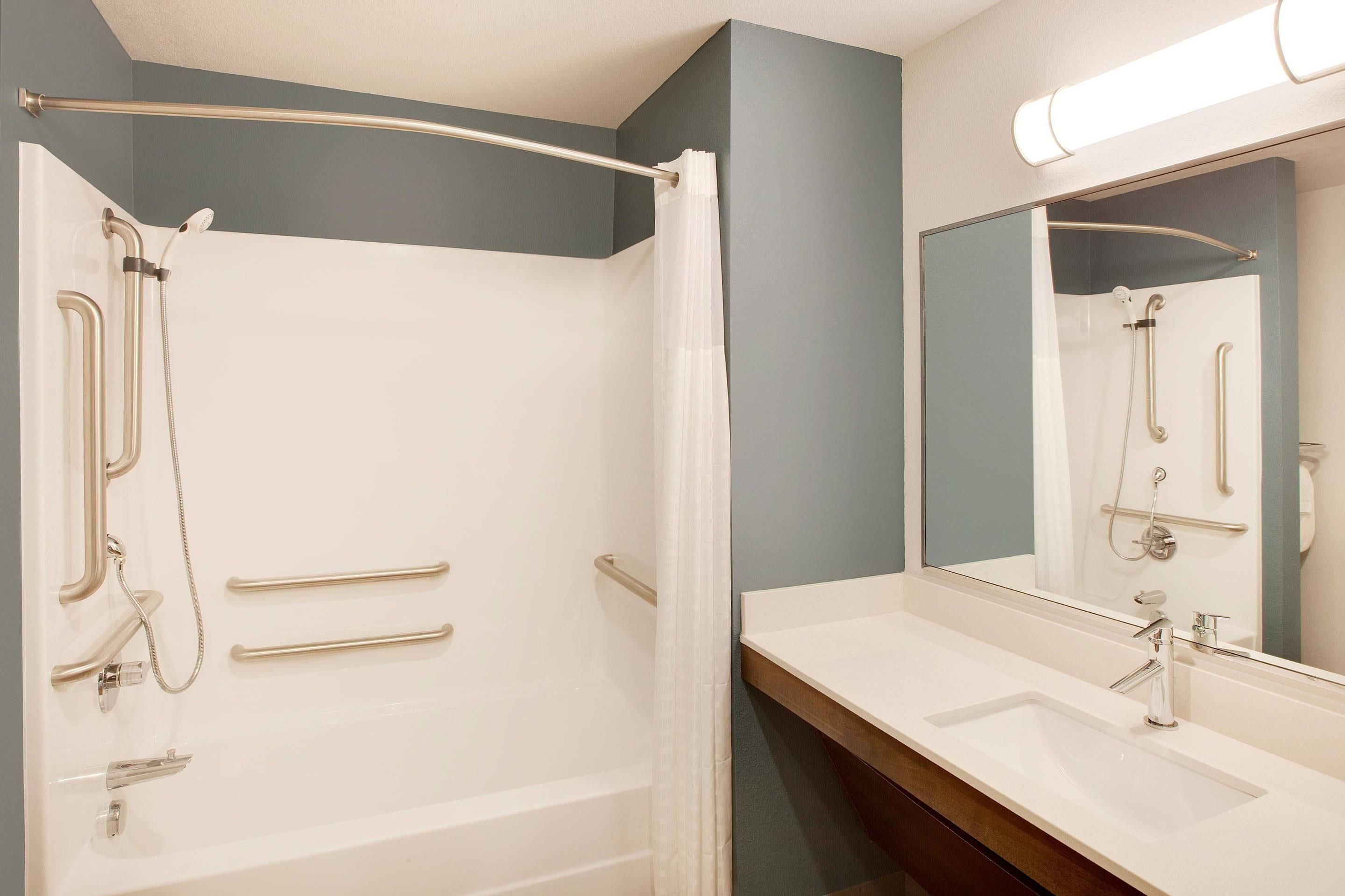 A bathroom with a walk-in shower, grab bars, a sink with a mirror, and a towel rack.