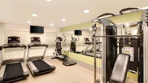 Ein Fitnessraum mit Laufbändern, Crosstrainern und einer Hantelbank.