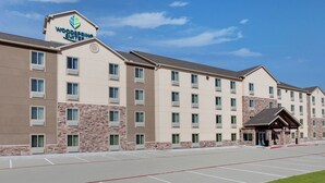 A multi-story hotel with a prominent sign reading "Woodspree Suites." It features a parking lot with marked spaces and a small grassy area in the foreground. - WoodSpring Suites Houston Northwest (Houston)