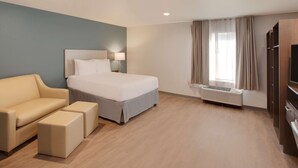 Ein Hotelzimmer mit Bett, Sofa, Fernseher und einem fenster mit Vorhängen.