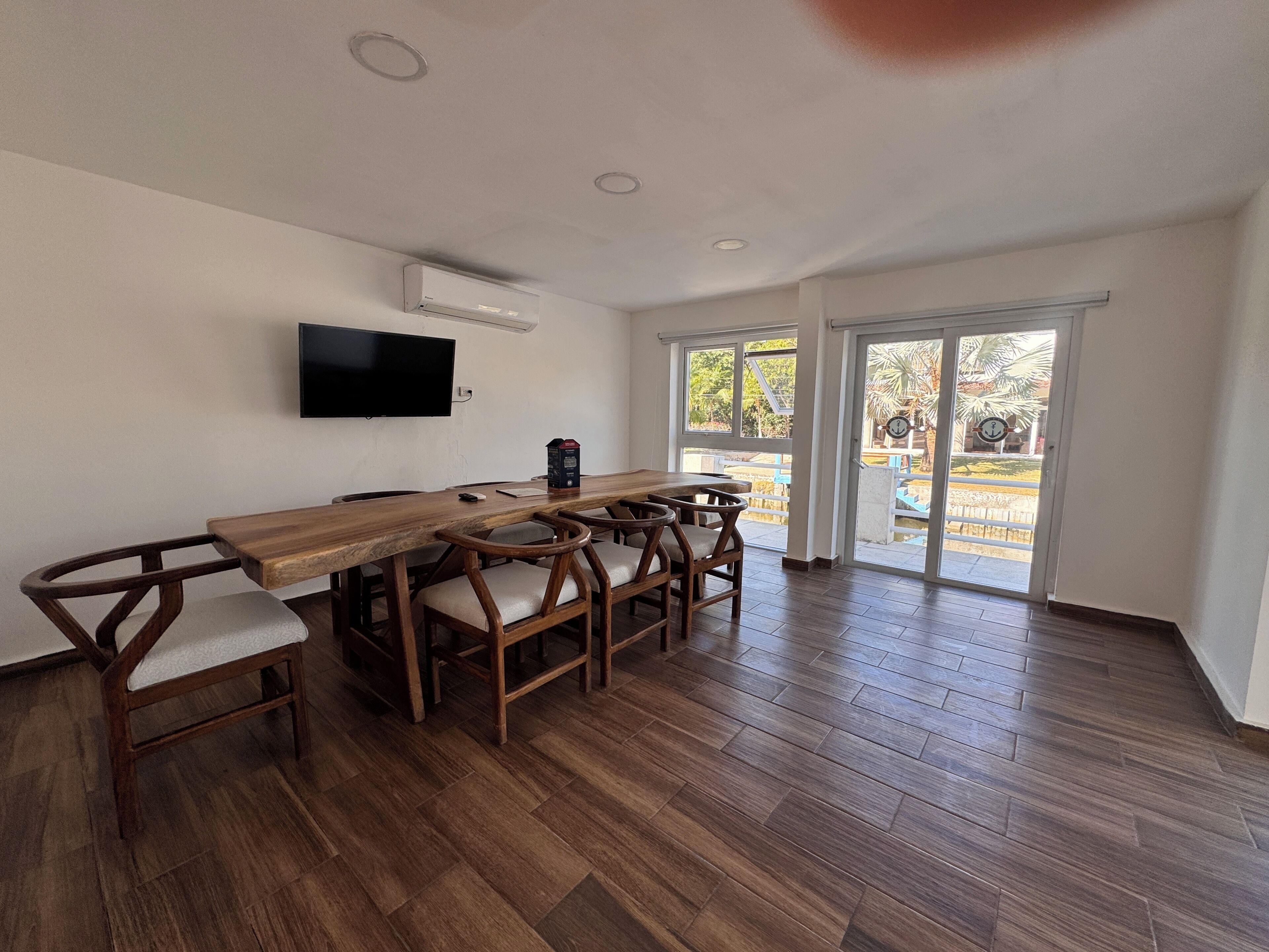 Un coin repas avec une table et des chaises en bois, un téléviseur à écran plat fixé au mur et une porte-fenêtre coulissante donnant sur un espace extérieur.