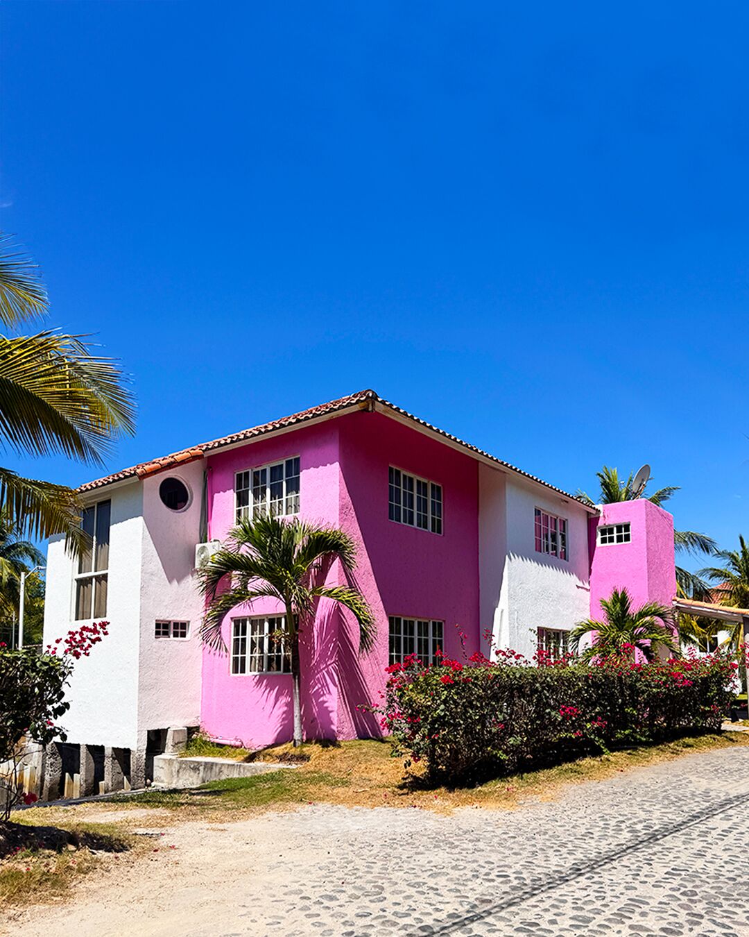 Un bâtiment rose avec un toit recouvert de tuiles, des fenêtres et une antenne parabolique.