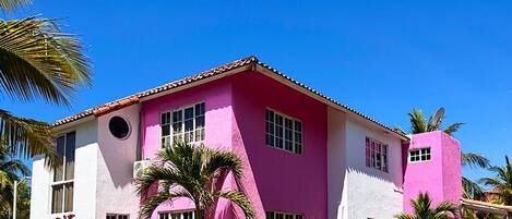 Un bâtiment rose avec un toit recouvert de tuiles, des fenêtres et une antenne parabolique.
