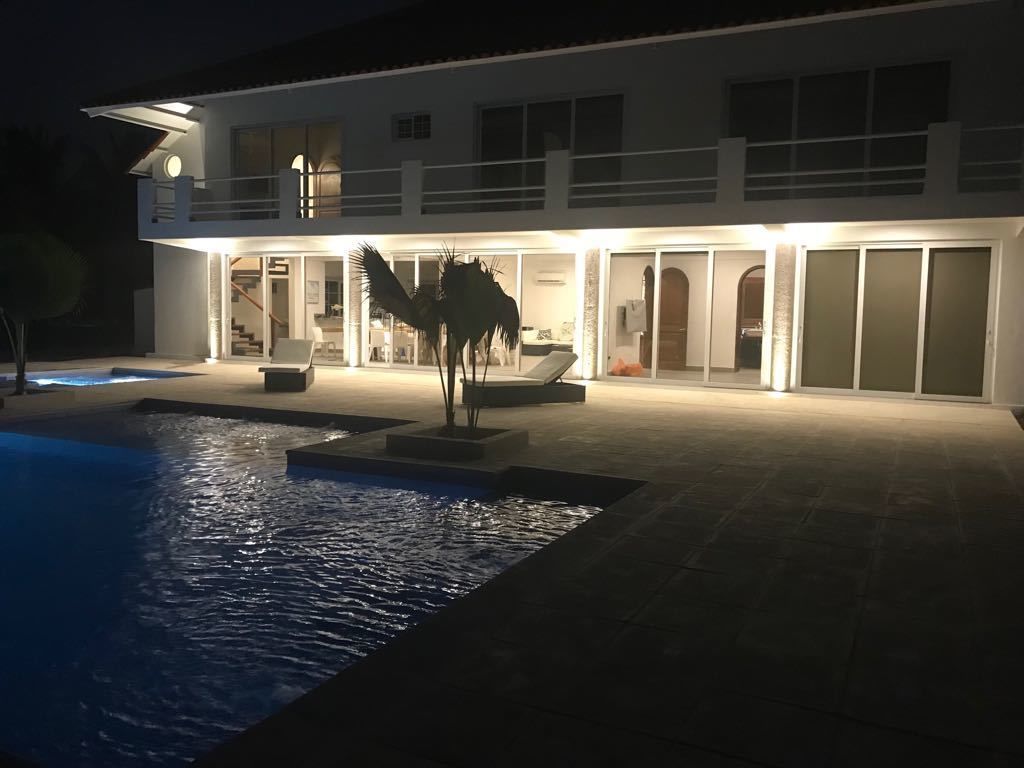 A modern house with a swimming pool, a covered patio, and a well-lit interior.
