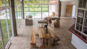 Een ruime binnenruimte met een grote houten tafel, bankjes en een rieten zobank.