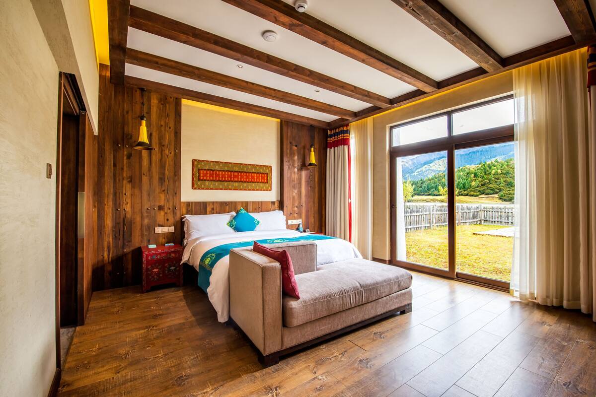Ein Schlafzimmer mit einem großen Bett, Holzbalken, Blick ins Freie und einer Schiebetür.