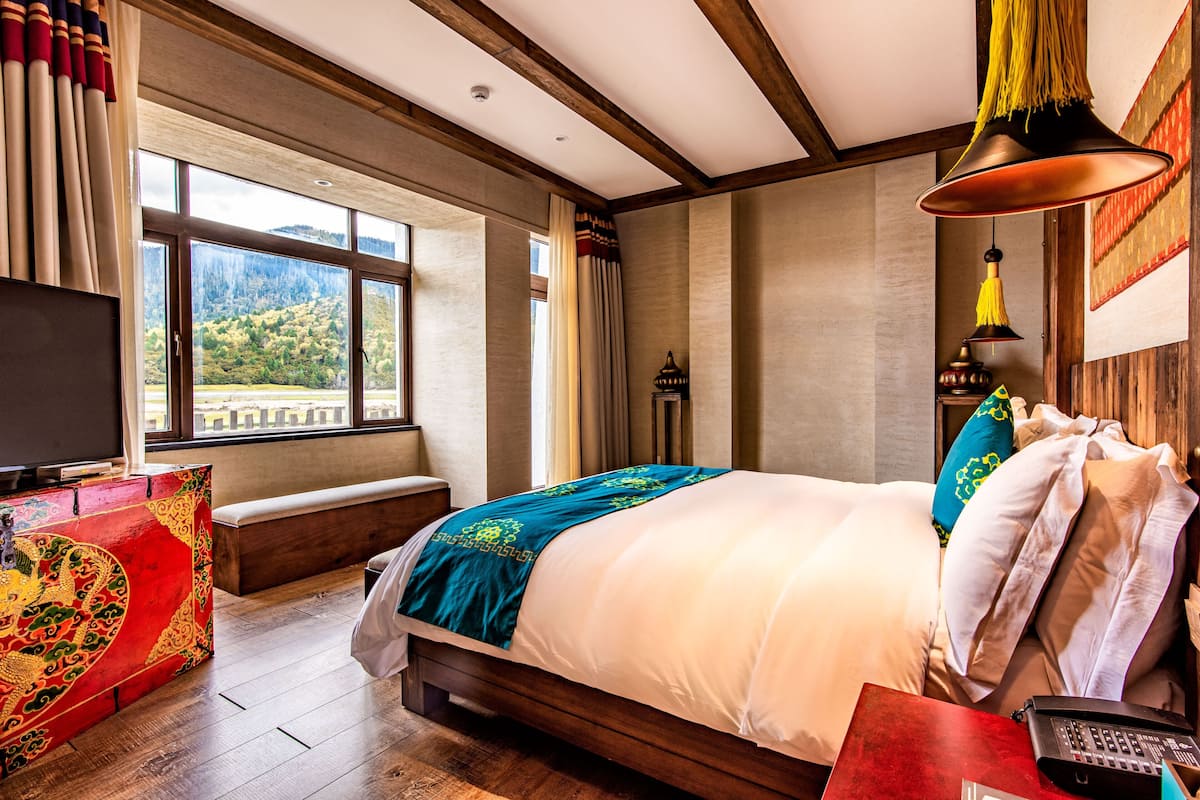 Ein Hotelzimmer mit einem großen Bett, einer Bank, einem Fernseher und Blick ins Freie.