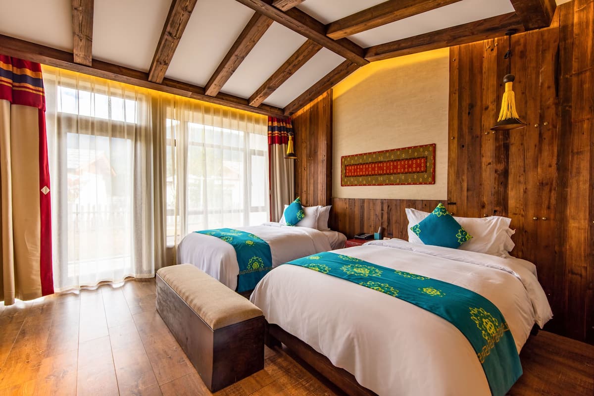 Ein Zimmer mit zwei Betten, Holzbalken an der Decke, einer Holzwand und einem großen Fenster mit Vorhängen.